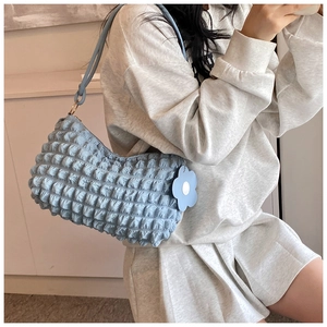 Detail of light blue bubble textured crescent shoulder bag with floral charm accessory