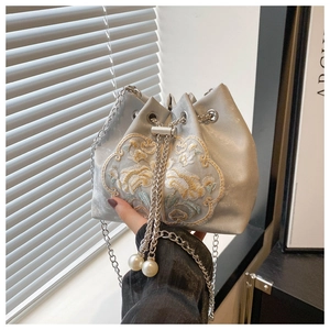 Detailed embroidery and large pearl accents on a silver bucket bag with chain strap