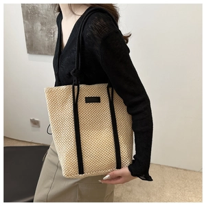 Detail of a large straw tote bag with black straps worn by a model for a beach vacation look