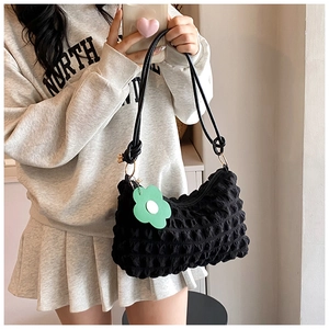 Detailed texture of black bubble pleated fabric shoulder bag with a green flower charm