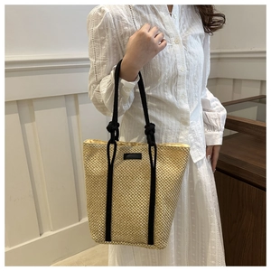 Detail view of woven straw tote bag featuring black rope handles and minimalist patch