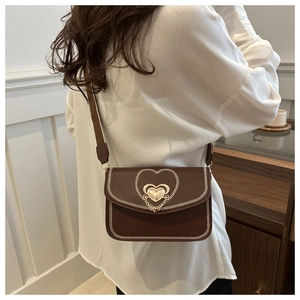 Detail of a brown crossbody bag with heart buckle and contrast stitching on a model