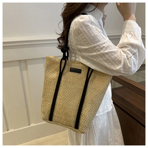 Detail of large woven straw tote bag with black rope handles for beach holiday