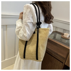 Detail of handwoven straw tote bag with black rope handles and minimalist summer texture