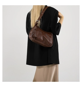 Dark brown leather crescent saddle bag styled on a model in a black blazer and skirt