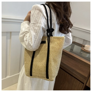 Detail of beige straw tote bag with black rope handles held by a woman in white dress