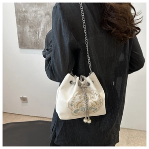Detail of embroidered floral bucket bag with chain strap and pearl tassels on a model