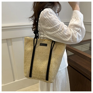 Detail of hand-woven straw tote bag with black rope handles and minimal leather patch