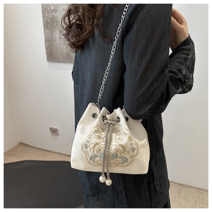 Détail du sac seau en satin blanc avec broderie florale et élégants pompons en perles