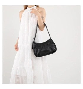 Detail of black pleated half-moon shoulder bag styled with a white sleeveless lace dress