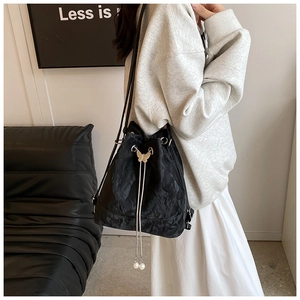 Detail of black drawstring bucket bag with gold butterfly hardware and pearl charms