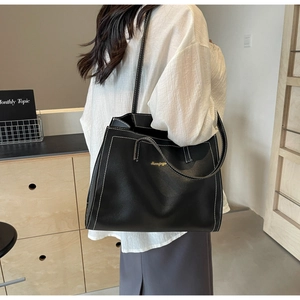 Detail of black tote bag with white contrast stitching and gold logo on leather