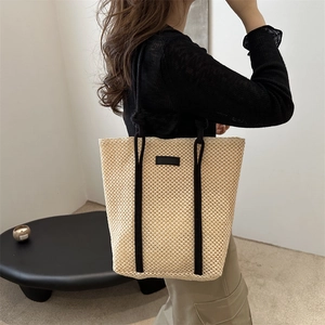 Minimalist straw tote bag with black handles shown in a lifestyle indoor setting