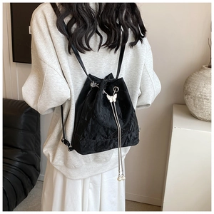 Detail of black wrinkled texture bucket bag featuring a silver butterfly and pearl tassel