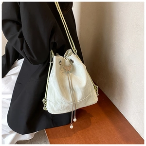 Detail of light green bucket bag with silver butterfly charm and pearl drawstrings