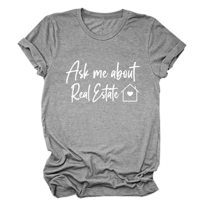 Dettaglio di una t-shirt grigia con scritta 'Ask me about Real Estate' e icona di casa