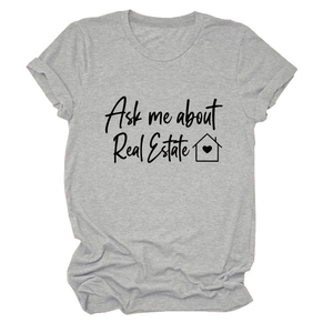 Dettaglio della maglietta grigia girocollo con scritta 'Ask me about Real Estate' e casa