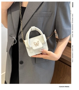 Close-up of a white mini handbag featuring a pearl butterfly buckle and gold chain strap