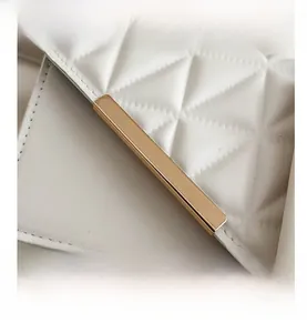 Detail of white quilted faux leather bag with stitching and gold metal accent