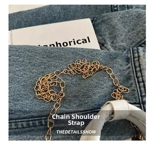 Detail of golden metal chain strap connected to white leather handle on denim background
