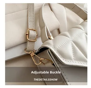Macro detail of golden metal adjustment buckle and quilted leather strap on white handbag