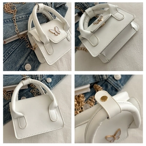 Macro detail of white leather handbag featuring butterfly hardware and gold chain strap
