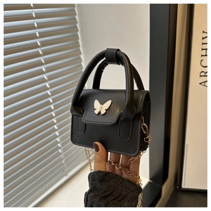 Close-up of black mini box bag featuring a white butterfly ornament and golden chain strap