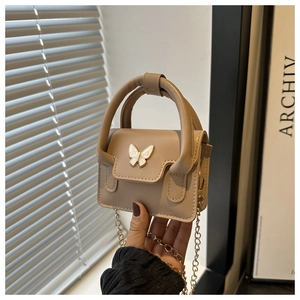 Detailed shot of nude leather mini bag featuring an elegant white butterfly clasp and chain