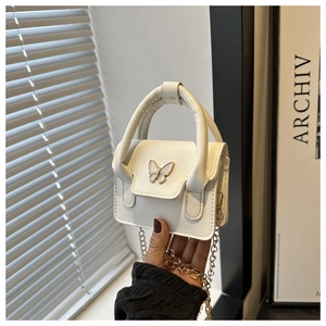 Detail of white mini handbag featuring butterfly metal accent and gold chain strap