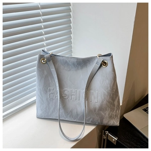 Detail of grey-blue tote bag featuring embossed FASHION lettering and thin shoulder straps