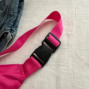 Detalle de la hebilla de plástico y correa de lona rosa de la riñonera deportiva multi