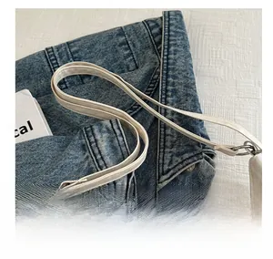Detail of white PU leather shoulder bag with metallic rings on denim background