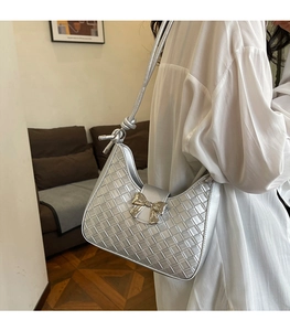 Silver woven underarm bag with bow metal buckle shown on a white shirt in detail