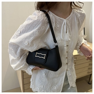 Sac sous le bras noir chic avec boucle dorée sur un mannequin portant un haut en dentelle