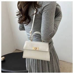 Detail of cream croc-embossed handbag with gold twist lock and adjustable shoulder strap