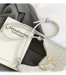 Detail of silver woven shoulder bag with metallic bow and sleek round strap handle