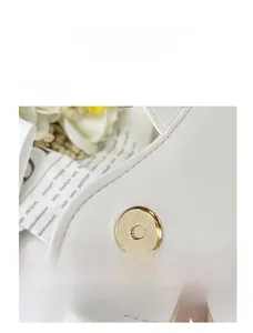 Detailed close-up of premium golden magnetic buckle and neat stitching on white leather bag