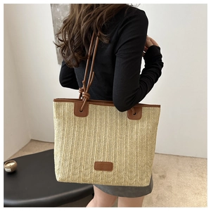 Detail of straw tote bag showing brown leather handles and brand logo patch texture