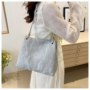 Detail of grey pleated tote bag with embossed Fashion text on shoulder of model