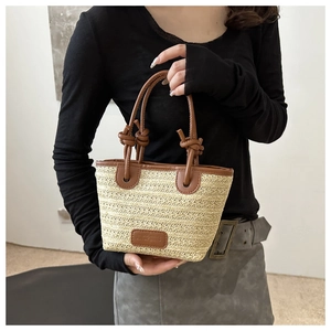 Detail of woven straw tote bag featuring brown leather handles and decorative knot detail