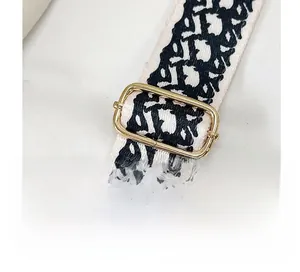 Detail of adjustable gold buckle on white and black oblique patterned bag strap