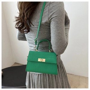 Detail of vibrant green crocodile embossed leather crossbody bag with golden clasp