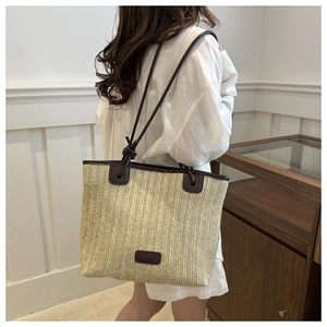 Detail view of large straw tote bag with woven texture and brown leather straps