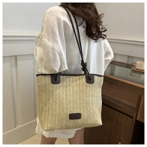 Straw tote bag with brown leather straps shown on a model in a minimalist setting