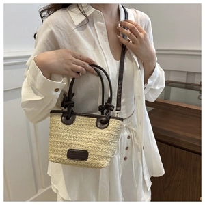 Detail of straw woven tote with brown leather handles and a minimalist metal logo plate