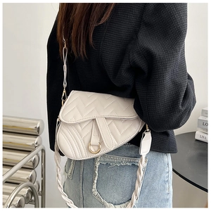 Detail of a beige saddle bag with V-shaped quilting and a woven shoulder strap