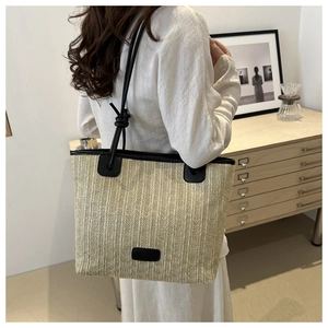 Detalle de un bolso de paja trenzada beige con ribetes de cuero negro en una modelo