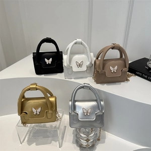 Glossy mini handbag with enamel butterfly buckle and chain strap on studio steps