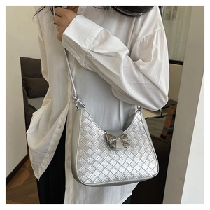 Detail of silver woven crescent bag with metallic bow buckle on slim shoulder strap