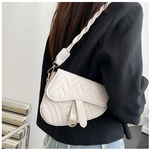 Detail of white quilted saddle bag with braided strap and golden D-ring hardware